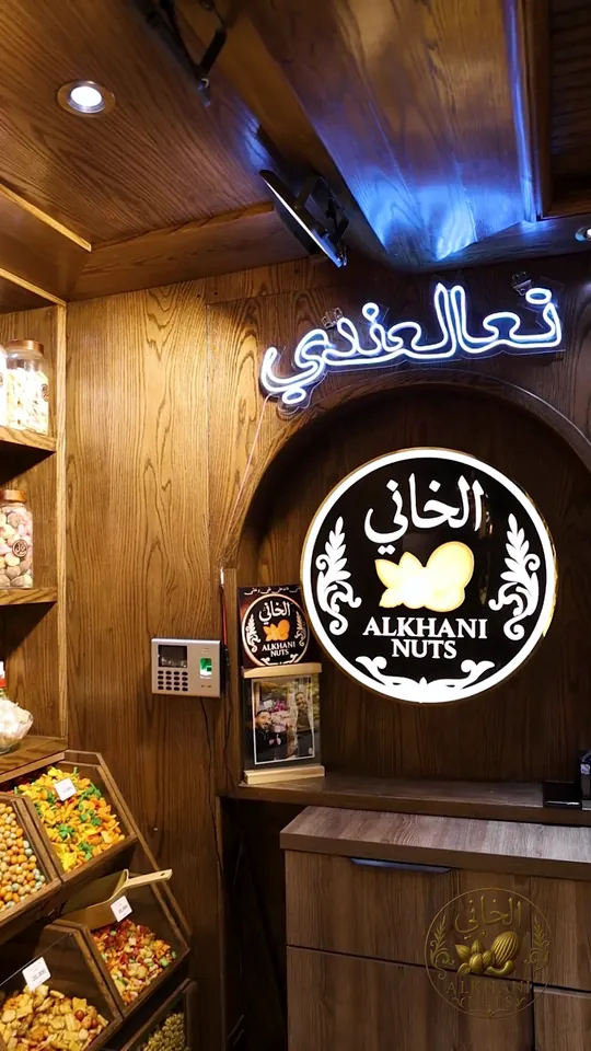 كلمة «تعالعندي» بنيون أبيض على خشب غامق، وتحتها لوحة سودا مدوّرة مكتوب عليها «الخاني»، بفرع دمسكينو